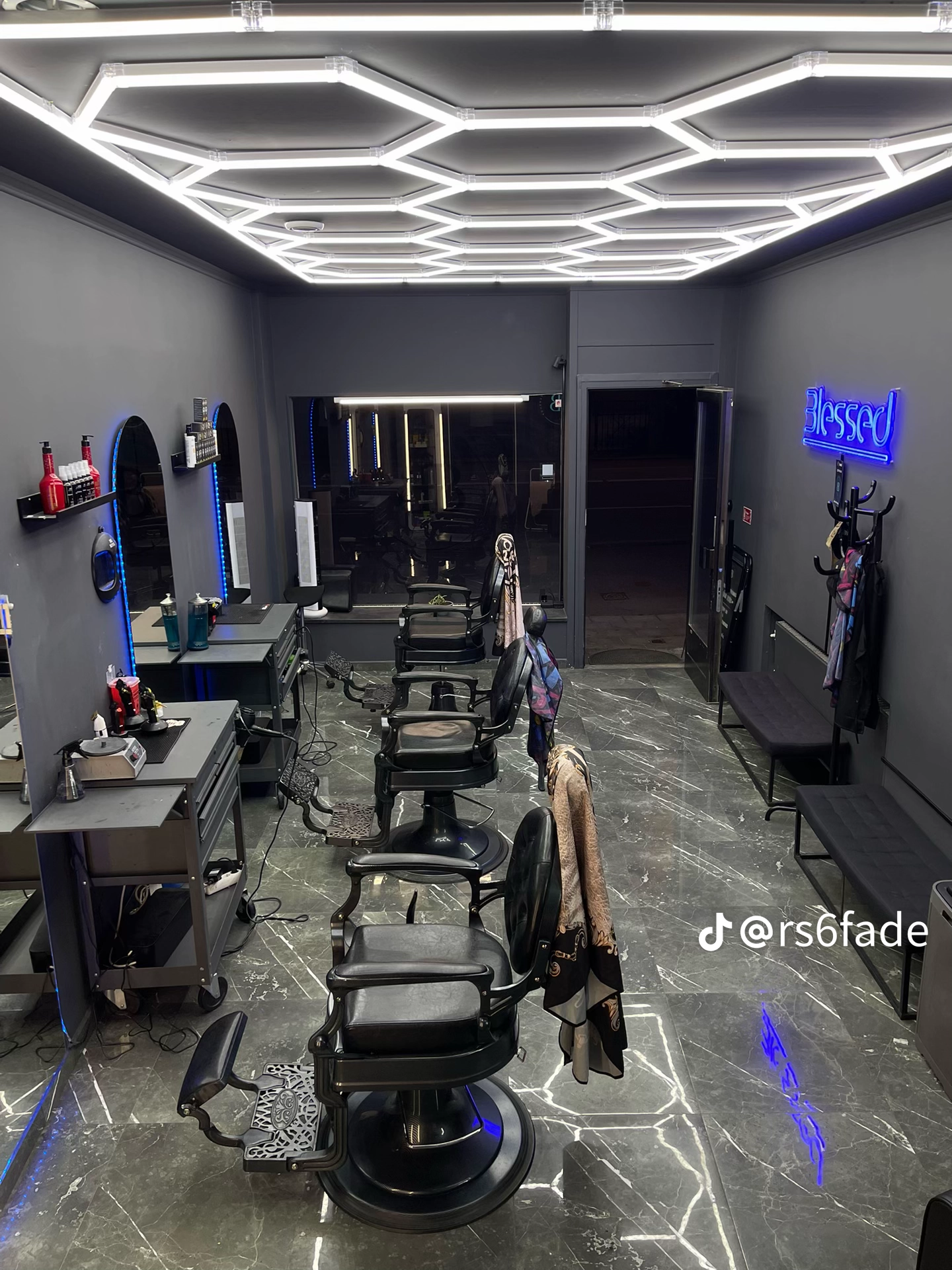 Barberarstolar på grå marmorgolv under hexagonbelysning hos Blessed Barbershop